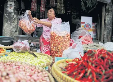  ??  ?? A vendor holds a bag of chilies for a customer at the morning market in Jakarta.