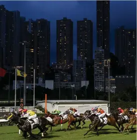  ??  ?? Horses and jockeys race under the Hong Kong skyscraper­s yesterday