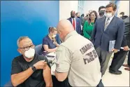  ??  ?? Florida Gov. Ron DeSantis, right rear, watches as Carlos Dennis, left, 65, rolls up his sleeve so that Miami-Dade County Fire Rescue paramedic, Capt. Javier Crespo, can administer a COVID-19 vaccine shot Monday at Jackson Memorial Hospital in Miami. [WILFREDO LEE/THE ASSOCIATED PRESS]