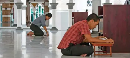  ??  ?? KUALA LUMPUR: A Malaysian Muslim man reads the Quran while the other prays at a mosque in downtown Kuala Lumpur, Malaysia yesterday. — AP