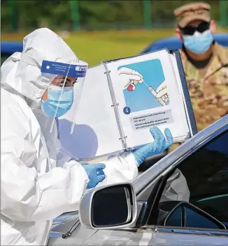  ?? CURTIS COMPTON / CURTIS.COMPTON@AJC.COM ?? A Walmart pharmacist shows how to do a self-swab as Georgia Army National Guard Pfc. Joshua Tucker looks on at a mobile COVID-19 drive-thru testing site serving rural areas. National Guard testing strike teams are part of Georgia’s effort.