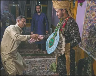  ??  ?? A Kashmiri man sprays sanitizer on the hand of Haseeb Mushtaq, a Kashmiri groom, as he arrives at his bride’s home on Sept. 14.