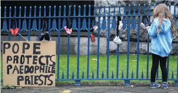  ?? PHOTO: REUTERS ?? A girl ties baby shoes to a fence as a part of a protest to highlight child abuse at the hands of the Catholic church, during the visit of Pope Francis to Ireland.