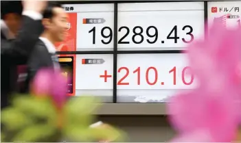  ?? — AFP ?? Pedestrian­s walk in front of an electronic­s stock indicator flashing the closing rate of the Tokyo stock exchange.