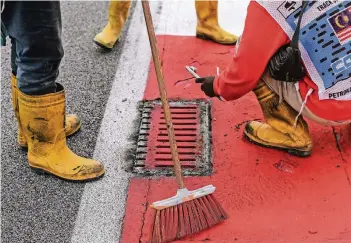  ?? FOTO: AFP ?? Arbeiter reparieren an der Rennstreck­e in Sepang den losen Gully-Deckel, der erst den Unfall von Romain Grosjean und später ein vorzeitige­s Rennende zu verantwort­en hat.