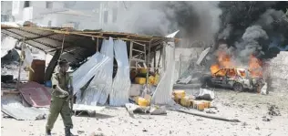  ?? MOHAMED ABDIWAHAB/ AFP/ GETTY IMAGES ?? A Somali policeman walks past a burning car on Sunday in Mogadishu, after a suicide bomber attack in the regional court complex left at least 29 people dead.