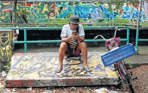  ?? Picture: REUTERS ?? BETWEEN A ROCK AND HARD PLACE: A migrant worker from Myanmar uses his phone at a street side in Bangkok, Thailand.