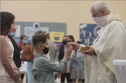  ?? DAVE ANGELL — FOR THE MACOMB DAILY ?? The Rev. Matt Ellis hands a communion host to a young man at St. Isidore Catholic Church in Macomb Township on Easter Sunday. The church had COVID-19restrict­ions in place, including masks, hand sanitation devices and social distancing.