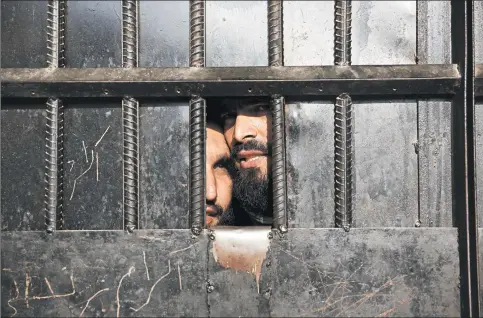  ?? RAHMAT GUL/AP ?? Taliban prisoners watch through the door inside a prison in August after an attack in the city of Jalalabad, east of Kabul, Afghanista­n.