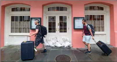  ?? The Associated Press ?? FRENCH QUARTER: People walk past Brennan’s restaurant in the French Quarter with sandbags on the front door as bands of rain from Tropical Storm Barry from the Gulf of Mexico move into New Orleans, La., on Friday.