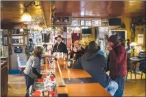  ??  ?? Leo Martel, the owner of the Keno City Hotel, in photo at left, stands at the end of his bar. Jim Milley, second from left in photo at right, is shown with guests at his Sourdough Cafe in Keno City. “He backed into a liquor license,” Milley said of...