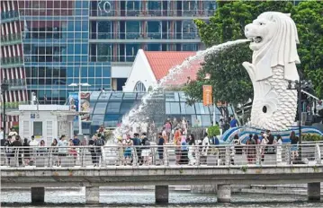  ?? — AFP ?? Changing landscape: People gather around the Merlion statue in singapore. The country rebounded from the pandemic, but is expected to face tougher going in the future.