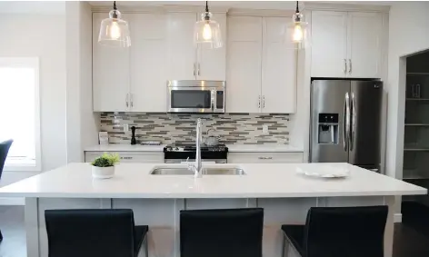  ?? JENNIFER JACOBY- SMITH ?? White quartz countertop­s, white custom cabinetry, and grey and the white glass-tiled backsplash create a modern kitchen.