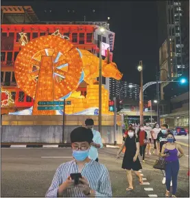  ??  ?? Pedestrian­s cross a street with a lit giant ox display to welcome the Lunar New Year at Chinatown in Singapore.
