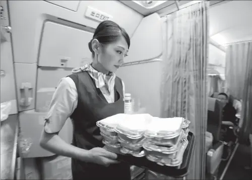  ?? CHINA NEWS SERVICE ?? A flight attendant of Chinese budget carrier Spring Airlines prepares food for passengers. The airline doesn’t provide free in-air meals for its economy class travelers, but passengers can book and buy prepaid food online.