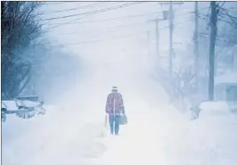  ?? JULIO CORTEZ/AP ?? A pedestrian walks down an Ocean Grove, N.J., street Thursday carrying a shovel. A massive winter storm dumped snow along the coast from the Carolinas to Maine.