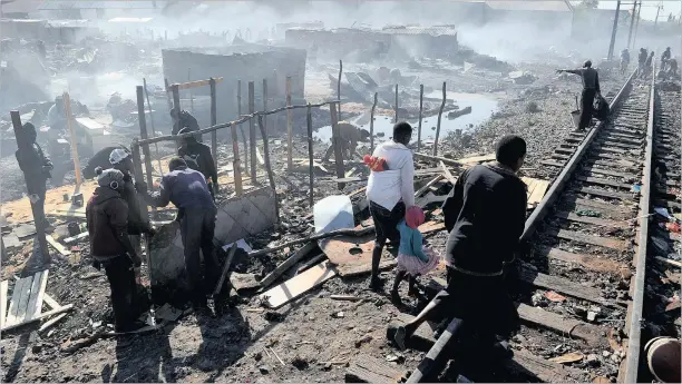  ?? PICTURE: CHRIS COLLINGRID­GE ?? AFTERMATH: Residents of the Mangolongo­lo informal settlement start to rebuild the shacks that burnt down next to the railway line in Denver early this morning.