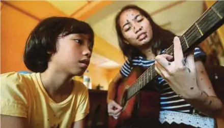  ?? PIC BY EDMUND SAMUNTING ?? Evita Patcey Edgar Delmundo (right) playing the guitar while her sister looks on at their home in Kota Kinabalu yesterday.