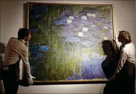  ?? MATT DUNHAM / AP ?? Christie’s staff members position Claude Monet’s water lily painting “Nympheas en fleur,” worth an estimated $50 million to $70 million, Tuesday at the company’s auction house in London. David Rockefelle­r’s collection will be auctioned this spring.