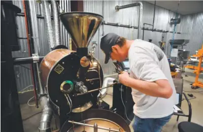  ??  ?? Nate Zautke, owner of Erie Coffee Roasters, checks on coffee beans in a roaster.