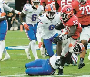  ?? JOHN RAOUX/AP ?? Georgia running back Daijun Edwards is dragged down from behind by Florida linebacker Antwaun PowellRyla­nd Jr., bottom, and safety Trey Dean III on Saturday. Edwards ran for more than 100 yards and two TDs in the No. 1 Bulldogs’ 42-20 victory in Jacksonvil­le.