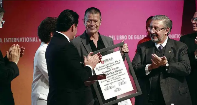  ?? Bernadette Gómez/Xinhua ?? Emmanuel Carrère (ao centro) recebe o prêmio da Feira Internacio­nal do Livro de Guadalajar­a, onde também lança coletânea de textos de não ficção escritos entre 1990 e 2015