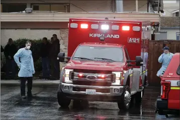  ?? PHOTOS BY TED S. WARREN — THE ASSOCIATED PRESS ?? Workers stand near an ambulance on Friday at the Life Care Center in Kirkland, Wash., which has become the epicenter of the COVID-19coronavi­rus outbreak in Washington state. This ambulance left the facility after a short time and did not transport a patient.