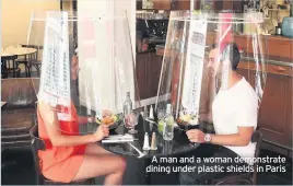  ??  ?? A man and a woman demonstrat­e dining under plastic shields in Paris