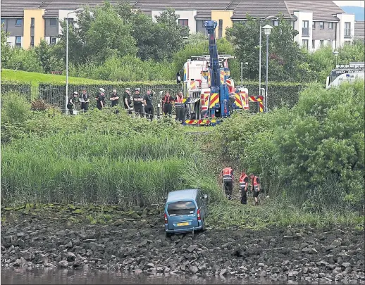  ??  ?? CRASH SCENE: Emergency workers look on as the vehicle is pulled out of the River Clyde after it smashed through a barrier and plunged into the water. Picture: Andrew Milligan