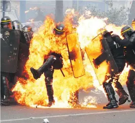  ?? ZAKARIA ABDELKAFI/AFP/GETTY IMAGES ?? French anti-riot police officers are engulfed in flames as they face protesters during a march for the annual May Day workers’ rally in Paris Monday.