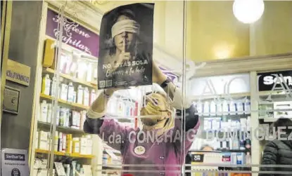  ?? S. GARCÍA ?? Una trabajador­a de una farmacia cuelga el cartel de la campaña. ▷