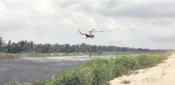  ?? – Photo by Jenifer Laeng ?? Bomba’s Mi17 helicopter scoops water from the Baram River for a water bombing run.