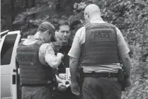  ?? Associated Press ?? ■ Washington State Fish and Wildlife police confer with a King County Sheriff's deputy Saturday on a remote gravel road above Snoqualmie, WA., following a fatal cougar attack. One man was killed and another seriously injured when they encountere­d a...