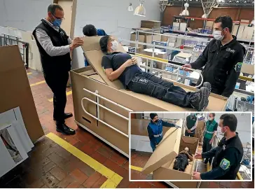  ?? AP ?? Rodolfo Gomez, left, and his employees demonstrat­e how their design of a cardboard box can serve as both a hospital bed and a coffin, designed for Covid-19 patients, in Bogota, Colombia.