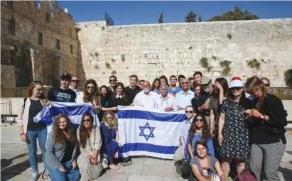  ?? (Marc Israel Sellem/The Jerusalem Post) ?? DEPUTY FOREIGN MINISTER Tzipi Hotovely (standing behind left corner of flag) and the three paratroope­rs from David Rubinger’s iconic 1967 photo (in white shirts) pose with internatio­nal students at the Western Wall on Thursday.