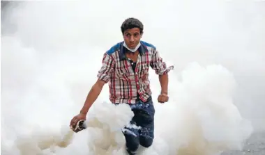  ?? Photo: REUTERS ?? Political haze: A protester is about to return a tear-gas canister hurled by riot police during democracy clashes in Cairo.