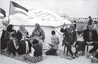  ??  ?? A family sits in front of their tent east of Gaza City. They have hung up signs of the names of their original villages to which they hope to return. Palestinia­ns have set up tents along the border with Israel and will carry out a six-week sit-in...