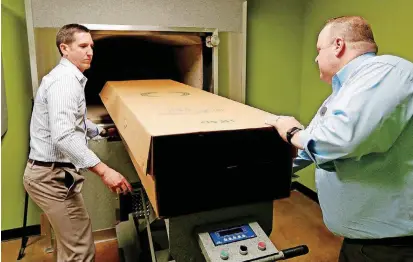  ?? [PHOTO BY PAUL HELLSTERN, THE OKLAHOMAN] ?? Jason Mayes, left, and owner Darin Corbett demonstrat­e how a cardboard coffin insert is prepared to undergo the cremation process at Oklahoma City Cremation.