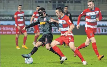  ?? FOTO: STEFAN PUCHNER/DPA ?? Heidenheim­s Andreas Geipl (Mitte) und Regensburg­s Albion Vrenezi, der Mann mit der Maske, kämpfen um den Ball, Tobias Mohr (rechts) schaut zu.