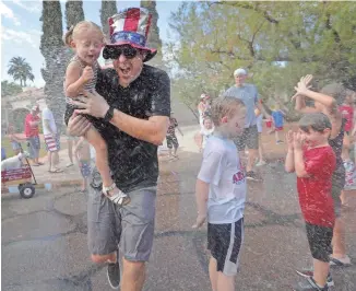  ?? PHOTOS BY MICHAEL CHOW/THE REPUBLIC ?? David Kohne runs with his daughter Rosie through water during the Arcadia Fourth of July parade in Phoenix. This is the 23rd year of the community event.