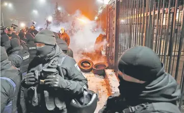  ?? — AFP photo ?? A National Guard serviceman extinguish­es a torch thrown by a protester during a rally in front of the Russian embassy in Kiev.