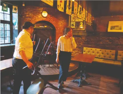  ?? CHRISTINNE MUSCHI ?? Teagan Kum-sing, right, and Zach Oskrdal put chairs away at Hurleys Irish Pub, which closed its doors yesterday because of the government mandate to shut down bars in the hope of preventing the spread of the novel coronaviru­s.