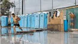  ?? REBECCA BLACKWELL/AP ?? Men bathe in a flooded shower and toilet area Thursday at a sports complex sheltering 6,150 Central American migrants, with 1,068 of those being children, in Tijuana, Mexico.