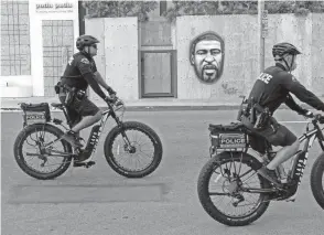  ?? KYLE GRILLOT/AFP VIA GETTY IMAGES ?? Police officers ride bicycles past a mural of George Floyd during a protest in Los Angeles in 2020.