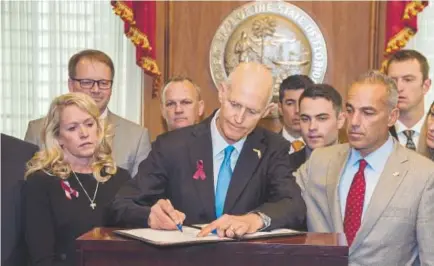  ?? Mark Wallheiser, AP ?? Florida Gov. Rick Scott signs the Marjory Stoneman Douglas Public Safety Act Friday at the state capitol in Tallahasse­e. Scott is flanked by the victims' parents Jennifer Montalto, left, Ryan Petty, second from left, and Andrew Pollack, right.