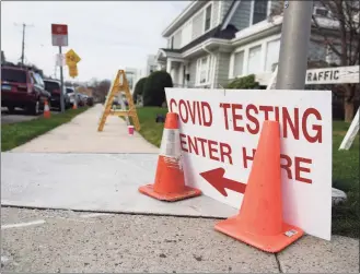  ??  ?? Above, Yesenia Pinto helps patients check in as they wait in their cars to be tested for COVID-19 at Community Health Center in Stamford on Wednesday. At left, a sign directs patients to the testing line. Community Health Center’s COVID-19 testing line has stretched around the block with patients often waiting several hours.