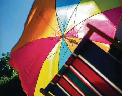  ?? FOTO: ARNO BURGI, DPA ?? Ein bunter Sonnenschi­rm und ein Liegestuhl stehen in einem Garten. Was ist deine Lieblingsf­arbe?