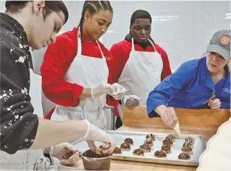  ?? STAFF PHOTOS BY CHRIS CHRISTO ?? A TASTE FOR LEARNING: Students, from left, Daniel Correia, Kiana Wilkerson and Olson Alexis make chocolate-dipped coconut macaroons with chef Carolynn Parmenter at the Everett High School culinary arts program.