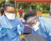  ?? THE' N. PHAM/STAFF ?? Tanyell Thomas, right, gives words of encouragem­ent to a teenager while Mariama Deenisie, left, waits to perform a nasal-swab test for COVID-19 at Geneva Square in Chesapeake June 5.