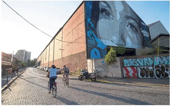  ?? — Photos: AFP ?? Cyclists pass a portrait of French boxer Sarah Ourahmoune by the street artist Marko 93, painted on the wall of the Halle Pouchard, a former industrial wasteland housing the ‘Grandes Serres de Pantin’ on the outskirts of Paris.